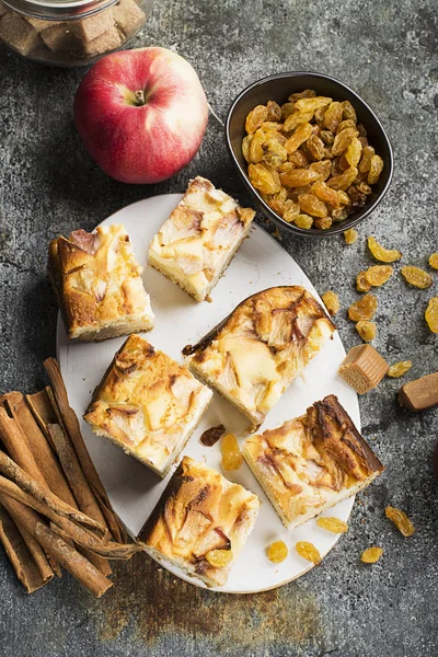 Uma torta caseira simples com maçãs e nata azeda em um fundo cinza com paus de canela, uma maçã, doces de caramelo. Vista superior. Foco seletivo . — Fotografia de Stock