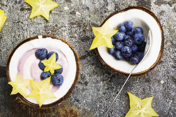 Een gezond ontbijt snack in helften van kokosnoot van berry yoghurt van twee kleuren met bosbessen en carambola's op een eenvoudige grijze stenen achtergrond. Bovenaanzicht. — Stockfoto