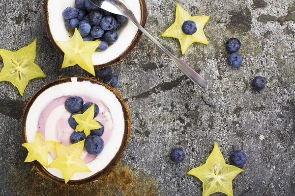 Un saludable snack de desayuno en mitades de coco de yogur de bayas de dos colores con arándanos y carambola sobre un simple fondo de piedra gris. Vista superior . — Foto de Stock