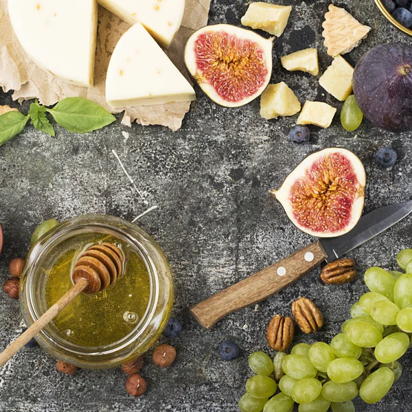 Cheese board for snacks, tricks, meetings with friends, on a gray stone background: assorted cheeses, young cheese, parmesan, cheese with fenugreek, figs, nuts, honey, grapes Top View.