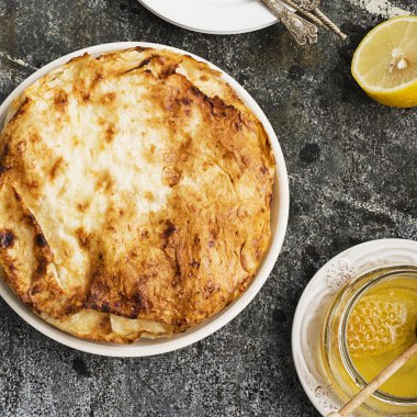 Yunan pasta irmik, süt, limon kabuğu, suyu, bal ve limon gri bir taş zemin üzerine pişirme için yuvarlak biçimde kremalı. Üstten Görünüm.