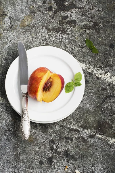 Saftig färsk nektarin på en vit platta med en vintage silver kniv på en grå sten bakgrund. Ovanifrån. — Stockfoto