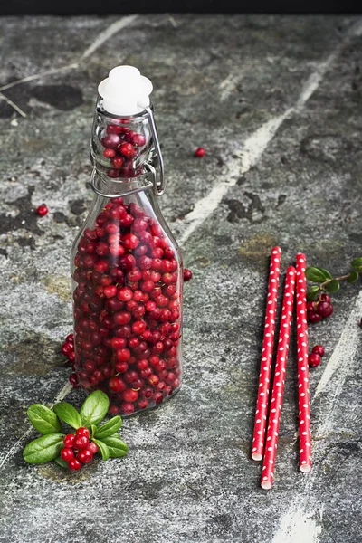 Flasche voller Beeren frische, reife Preiselbeeren aus dem Norden mit Strohhalmen für einen Cocktail. das Konzept gesunder Getränke aus Bioprodukten. Ansicht von oben. — Stockfoto