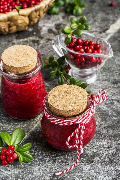 北方森林野生越桔，健康的有机饮食中分得的小玻璃小红莓酱罐与浆果和叶在灰色的石头背景上。选择性的焦点. — 图库照片