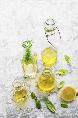 Bitkisel yağ, ayçiçeği ve zeytin ışık mermer zemin ile farklı boyutlarda dört şişe biber, adaçayı yaprakları ve fesleğen mutfak ve kozmetik kullanım için eklenmesi ile. Seçici odak.