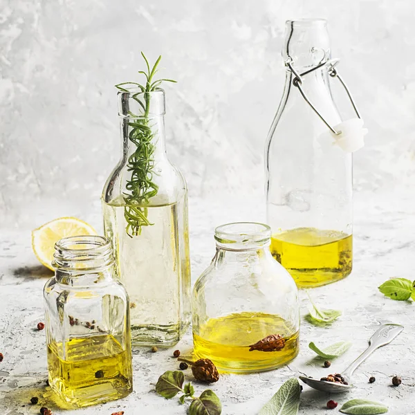 Quattro bottiglie di diverse dimensioni con olio vegetale, girasole e olive su fondo marmo chiaro con l'aggiunta di pepe, foglie di salvia e basilico per uso cucina e cosmetico. Focus selettivo . — Foto Stock