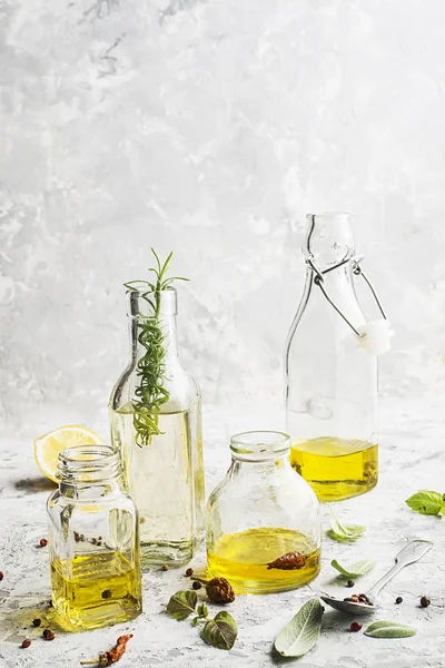 Vier Flaschen unterschiedlicher Größe mit Pflanzenöl, Sonnenblumen und Oliven auf hellem Marmorhintergrund mit Zusatz von Pfeffer, Salbeiblättern und Basilikum für Küche und Kosmetik. Selektiver Fokus. — Stockfoto