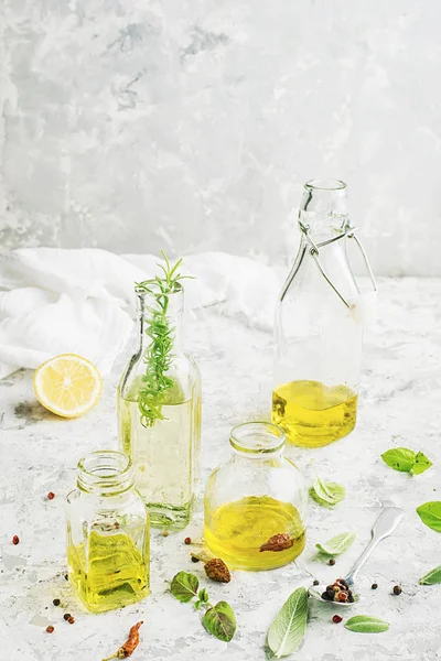 Quattro bottiglie di diverse dimensioni con olio vegetale, girasole e olive su fondo marmo chiaro con l'aggiunta di pepe, foglie di salvia e basilico per uso cucina e cosmetico. Focus selettivo . — Foto Stock