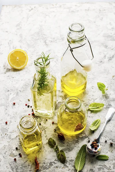 Quattro bottiglie di diverse dimensioni con olio vegetale, girasole e olive su fondo marmo chiaro con l'aggiunta di pepe, foglie di salvia e basilico per uso cucina e cosmetico. Focus selettivo . — Foto Stock