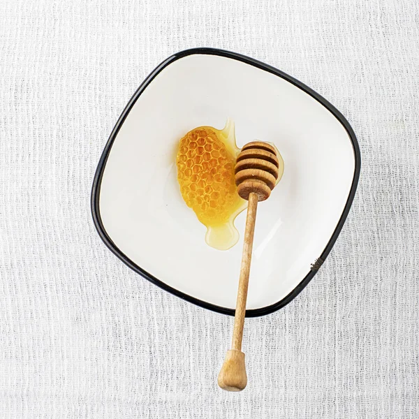 Uma cera feita por abelhas de favo de mel com mel fresco floral ou limão em uma tigela de aldeia simples esmaltada com um fuso para mel em um fundo cinza simples. Vista superior . — Fotografia de Stock