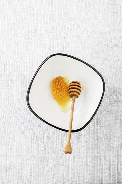 Uma cera feita por abelhas de favo de mel com mel fresco floral ou limão em uma tigela de aldeia simples esmaltada com um fuso para mel em um fundo cinza simples. Vista superior . — Fotografia de Stock