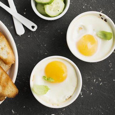 İki kişilik kahvaltı. Yumurta pişmiş fırında kızarmış ekmek ile seramik alakart formları ve taze salatalık dilimleri. Üstten Görünüm.