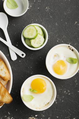 İki kişilik kahvaltı. Yumurta pişmiş fırında kızarmış ekmek ile seramik alakart formları ve taze salatalık dilimleri. Üstten Görünüm.