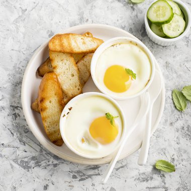 İki kişilik kahvaltı. Yumurta pişmiş fırında kızarmış ekmek ile seramik alakart formları ve taze salatalık dilimleri. Üstten Görünüm.