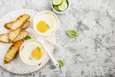 İki kişilik kahvaltı. Yumurta pişmiş fırında kızarmış ekmek ile seramik alakart formları ve taze salatalık dilimleri. Üstten Görünüm.