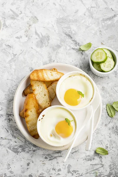 Petit déjeuner pour deux. Œufs cuits au four en portions de céramique avec pain grillé et tranches de concombre frais. Vue du dessus . — Photo