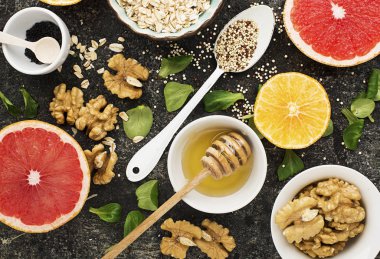 Koyu arka plan kırmızı yakut bir sağlıklı kahvaltı yemek için malzemeler kanlı greyfurt, yulaf gevreği, kinoa, yeşil yapraklar, ceviz, çiçek tatlım, portakal, siyah susam. Üstten Görünüm. Saf vegeta kavramı