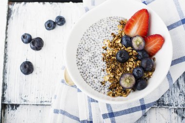 Sağlıklı kahvaltı snack ile bir puding chia tohum, granola, çilek ve böğürtlen hafif bir arka plan üzerinde beyaz bir tabak içinde. Yatay, yukarıdan görünüm.