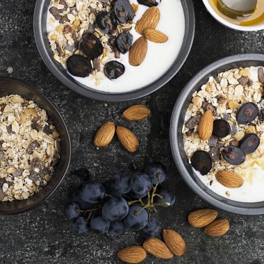 Kahvaltı sağlıklı mevsimlik malzemelerle: granola, pul, tatlım, kara üzüm, badem bir hizmet gri gri grunge arka plan üzerinde pial. Üstten Görünüm. Vejetaryen organik gıda kavramı.