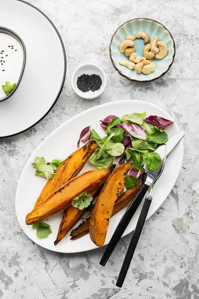 Rebanadas al horno de batatas para un almuerzo vegetariano saludable con ensalada, salsa de yogur, sésamo negro servido en un plato. Vista superior . —  Fotos de Stock