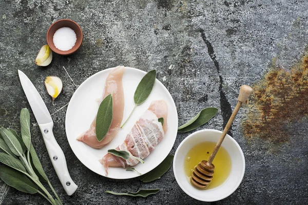 Petits poitrines de poulet aux feuilles de sauge, miel floral, sel, huile d'olive, ail, avec de fines lanières de bacon avant cuisson. Vue du dessus . — Photo