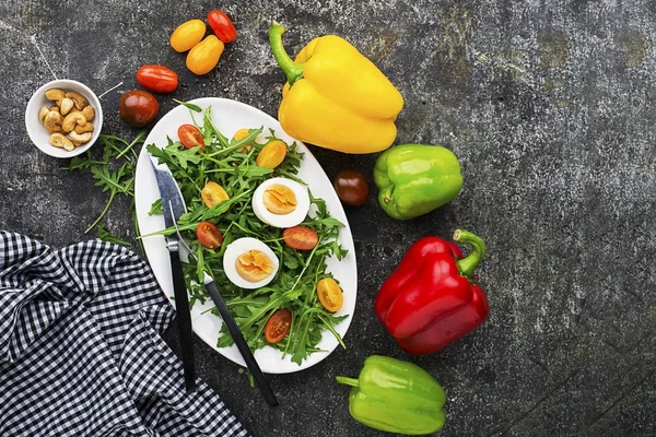 Весенний пасхальный салат со свежими овощами: помидорами, рукколой, яйцом, орехами и гренками на сером фоне гранжа. Вид сверху .. — стоковое фото