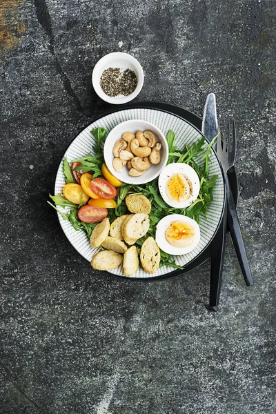 Salade de printemps fraîche avec œuf bouilli, roquette, salade, tomates, pacanes et croûtons de pain grillé croustillants dans un grand plat sur fond gris. Vue du dessus .. — Photo