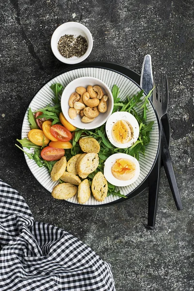 Salade de printemps fraîche avec œuf bouilli, roquette, salade, tomates, pacanes et croûtons de pain grillé croustillants dans un grand plat sur fond gris. Vue du dessus .. — Photo