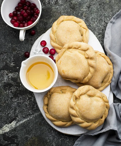 Bequemes Essen für die ganze Familie. hausgemachte Mini-Kuchen aus frischem einfachen Teig mit saisonalen Beeren, serviert mit Honig. Draufsicht auf grauem Grunge-Hintergrund. — Stockfoto