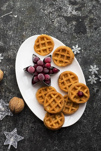 自制的软华夫饼早餐与冷冻浆果有机北莓在白色椭圆形的陶瓷盘上的灰色垃圾背景与银色圣诞装饰和花环。顶部视图. — 图库照片