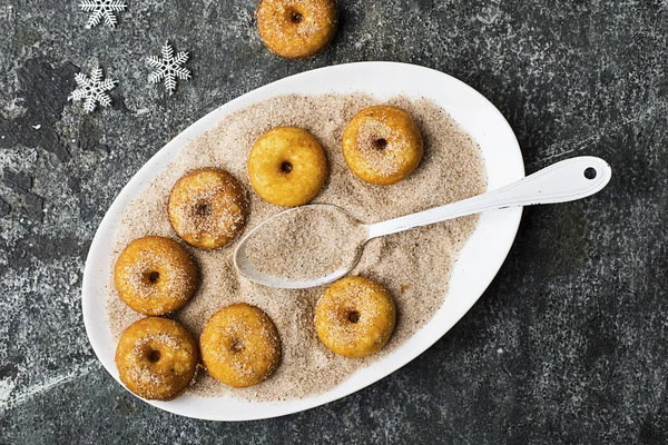 Aptitretande ruddy traditionella munkar med socker och kanel på en oval maträtt på en grå grunge trendiga bakgrund med en jul graciösa snygg inredning med silver stjärnor och en krans. Ovanifrån. — Stockfoto