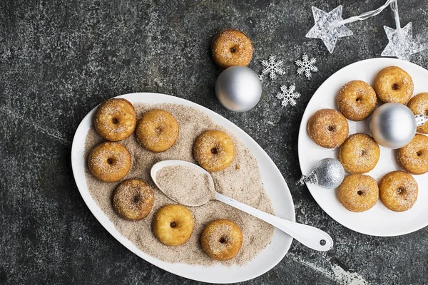 Smakelijk rossig traditionele donuts met suiker en kaneel op een ovale schotel op een trendy grijze grunge-achtergrond met een kerst sierlijke netjes interieur met zilveren sterren en een slinger. Bovenaanzicht. — Stockfoto
