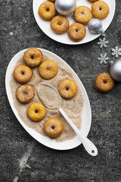 Donuts tradicionais rubicundos apetitosos com açúcar e canela em um prato oval em um fundo da moda grunge cinza com um Natal decoração elegante graciosa com estrelas de prata e uma grinalda. Vista superior . — Fotografia de Stock