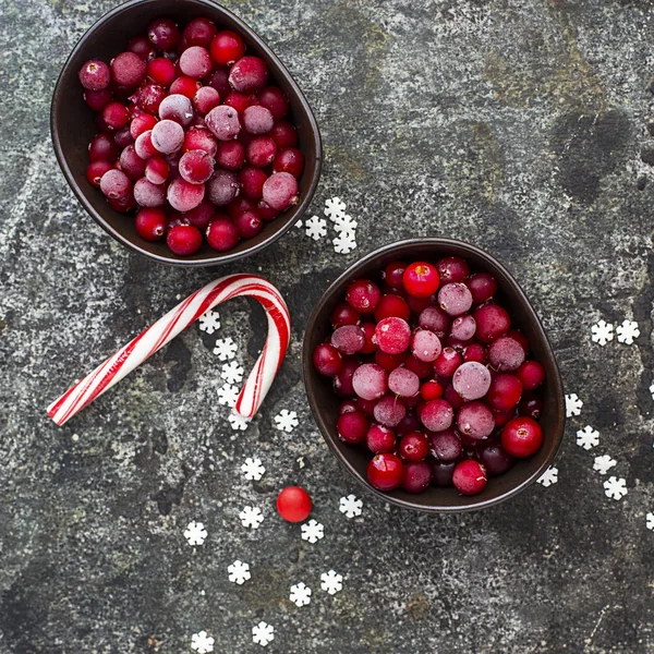 Bevroren cranberries in een wit geëmailleerde vintage kom op een effen grijze achtergrond met een geëmailleerde lepel van beau. Bovenaanzicht. — Stockfoto