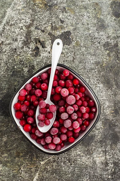 Frysta tranbär i en vit emaljerad vintage skål på en vanlig grå bakgrund med beau emaljerad sked. Ovanifrån. — Stockfoto