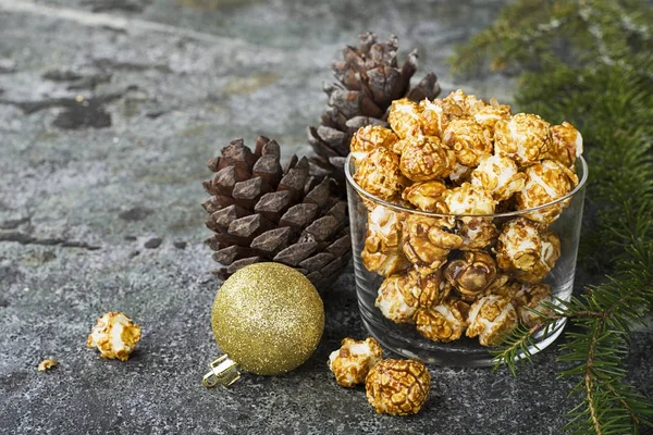 Smakelijk gouden caramel popcorn in papieren gestreepte cups in de New Year's interieur met spar kegels, New Year's gouden ballen op een grijze steen moderne achtergrond. Selectieve aandacht. — Stockfoto