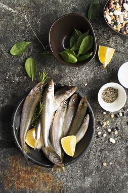 Fresh sea cold-water small fish such as smelt, sardine, anchovies on a simple background with fresh spinach, lemon slices, legumes for the concept of correct healthy natural nutrition. Top View. clipart