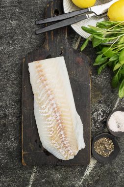 Kesme için bir mutfak bıçağı ile tuz, kara biber, taze mevsimlik Yeşiller, arka planda limon dilimleri ile sağlıklı sağlıklı yemek hazırlamak için taze deniz morina fileto. Kopya alanı.