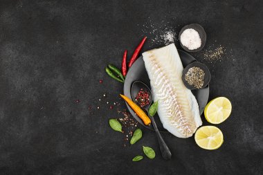 Pembe biber, acı biber, ıspanak, limon, basit bir siyah arka plan üzerine tuz ilavesi ile sağlıklı bir yemek hazırlanması için bir siyah seramik plaka üzerinde morina fileto. Üstten Görünüm. Kopya alanı.