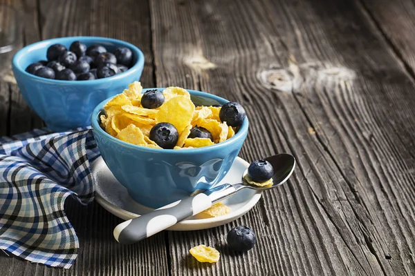 ホーム コーンフレークと青いセラミック磁器ボウルで簡単な木製の背景で新鮮なブルーベリーで健康的な朝食を料理の食材。選択と集中. — ストック写真