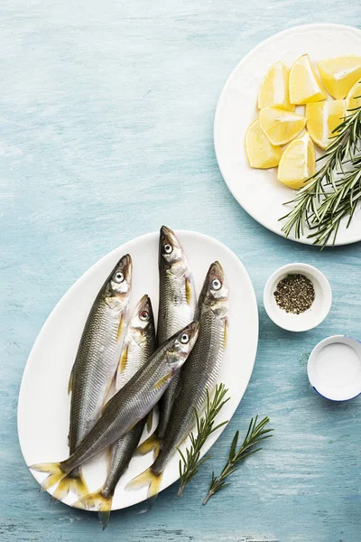 Petits poissons de mer frais éperlés, sardine sur fond simple avec du sel, du romarin et des tranches de citron. Vue de dessus. Le concept de fruits de mer sains , — Photo