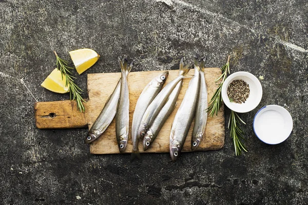 Petits poissons de mer frais éperlés, sardine sur fond simple avec du sel, du romarin et des tranches de citron. Vue de dessus. Le concept de fruits de mer sains , — Photo