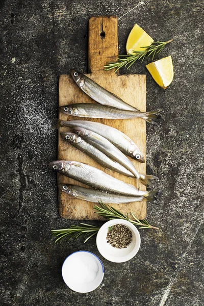 Pescado fresco de mar pequeño olía, sardina sobre un fondo simple con sal, romero y rodajas de limón. Vista superior. El concepto de comida marina saludable , —  Fotos de Stock