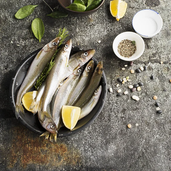 Petits poissons d'eau froide de mer fraîche tels que l'éperlan, la sardine, les anchois sur un fond simple avec des épinards frais, des tranches de citron, des légumineuses pour le concept de nutrition naturelle saine correcte. Vue du dessus . — Photo