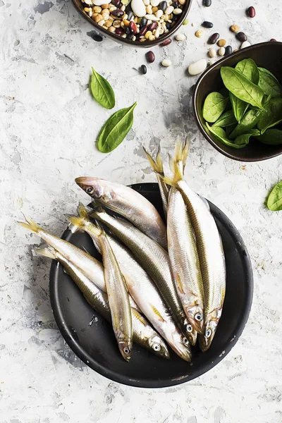 Fresh sea cold-water small fish such as smelt, sardine, anchovies on a simple background with fresh spinach, lemon slices, legumes for the concept of correct healthy natural nutrition. Top View.