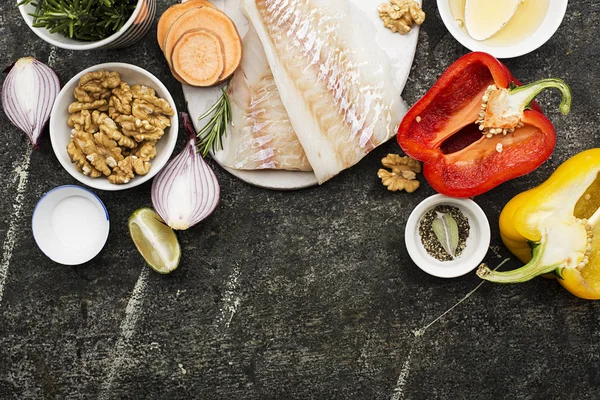 Torskfilé av torsk med färska grönsaker: paprika, rosmarin, Söt röd lök, mald peppar på en vit skärbräda på grunge grå bakgrund. Ovanifrån. Kopiera utrymme — Stockfoto