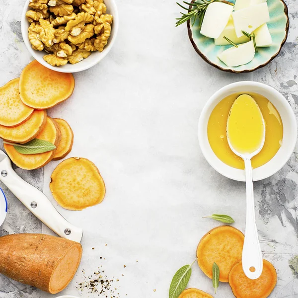 Ingredients for a healthy and comfortable diet: slices of fresh raw sweet potato, honey, walnuts, rosemary cheese, sage, salt on a light background using a sheet of parchment. Top View. Copy space