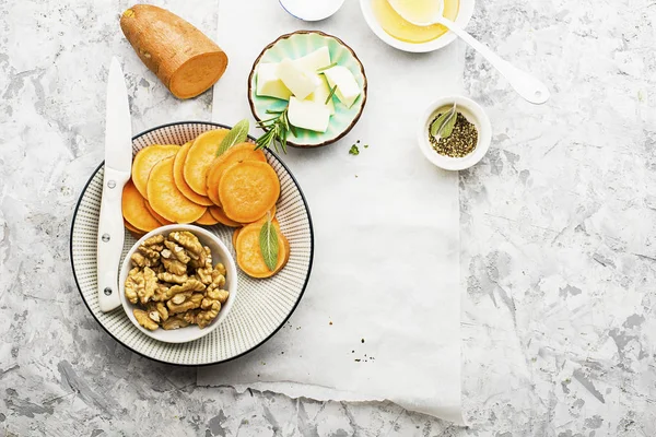 Ingredienser för en hälsosam och bekväm kost: skivor av färsk rå sötpotatis, honung, valnötter, rosmarin ost, salvia, salt på en ljus bakgrund med en ark av pergament. Ovanifrån. Kopiera utrymme — Stockfoto