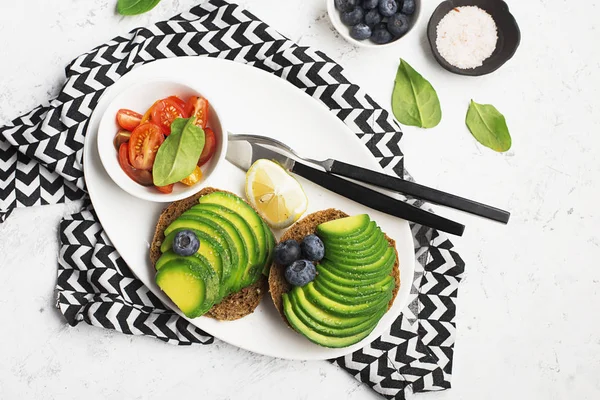 Smörgåsar för en hälsosam frukost med avokado och blåbär. Skivade körsbärstomater och spenat för servering. Ovanifrån. Kopiera utrymme. — Stockfoto