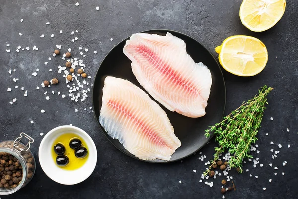 Healthy food ingredients. Fresh sea fish fillet, lemons, spices, salt, herbs, spices for a comfortable diet. Against a dark background. Top view.